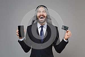 Overjoyed arabian muslim businessman in keffiyeh kafiya ring igal agal suit  on gray background. Achievement photo