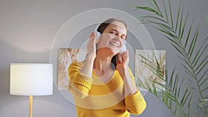 Overjoyed attractive woman in headphones smiling and dancing to the music enjoying beautiful melodies in comfort of her home