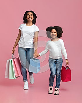 Overjoyed black woman and her cute daughter walking with shopping bags