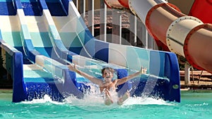 Overjoyed boy child going down by water slide aqua park extreme entertainment happy childhood slowmo
