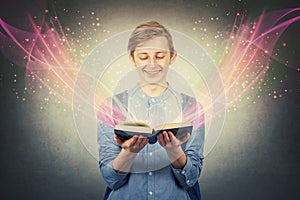 Overjoyed boy teenager smiling as holding a opened bewitched textbook. Magic book concept, different lights and glows telling an photo