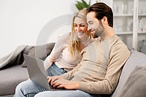 Overjoyed couple in love spending leisure time online with laptop at home. Blonde woman and man looking at the laptop