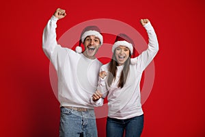 Overjoyed Couple In Santa Hats Emotionally Celebrating Success With Raised Fists