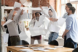 Overjoyed diverse employees throw papers celebrating success