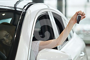 Overjoyed driver woman smiling and showing new key while sitting in car showroom