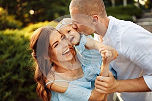 Overjoyed family walking at the park, loving mom hold smiling toddler in arms, laughing, caring dad kissing little