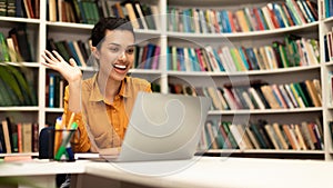 Overjoyed female teacher having online class using laptop and waving hand at webcamera, panorama with free space