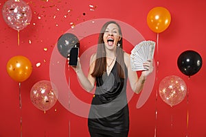 Overjoyed girl screaming hold mobile phone with blank empty black screen bundle lots of dollars cash money on bright red