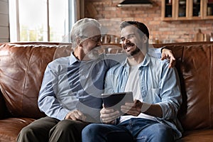 Overjoyed grownup son use tablet relax with senior son