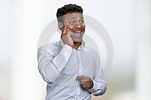 Overjoyed indian businessman talking on transparent phone against blurred background.