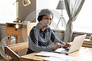 Overjoyed Indian girl in headphones laugh using laptop at home