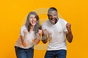 Overjoyed interracial couple celebrating success together, raising fists with excitement