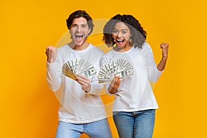 Overjoyed interracial couple holding lot of dollar cash, celebrating success together