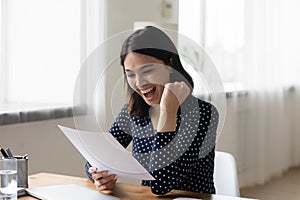 Overjoyed laughing Asian businesswoman celebrating achievement, reading letter