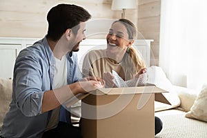 Overjoyed laughing millennial husband and wife unboxing packages after relocation