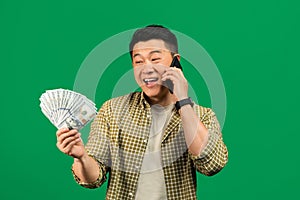 Overjoyed mature asian man holding dollar cash and talking on smartphone, lucky man emotionally reacting to online win