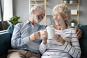 Overjoyed mature family couple laughing at jokes, drinking morning coffee.