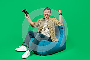 Overjoyed mature male gamer with joystick making YES gesture, feeling happy over victory, sitting in beanbag chair