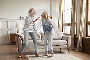 Overjoyed mature mother and adult daughter dance at home