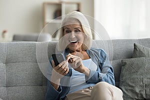Overjoyed mature woman sit on sofa gawp at cellphone screen