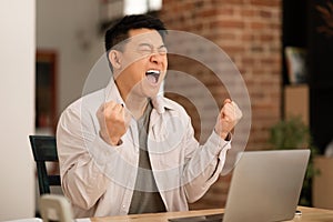 Overjoyed middle aged asian man using laptop and gesturing YES, feeling happy about online win or business promotion