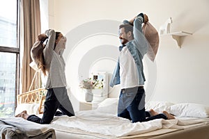 Overjoyed millennial couple have fun in pillow fight in bedroom