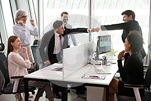 Overjoyed mixed race colleagues watching two teammates bumping fists.