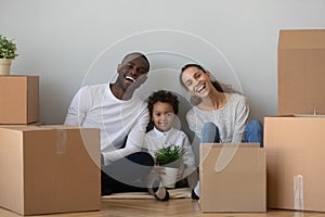 Overjoyed mixed race family sitting on floor near cardboard boxes.