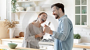 Overjoyed mixed race family spouse holding kitchenware, using as microphones.