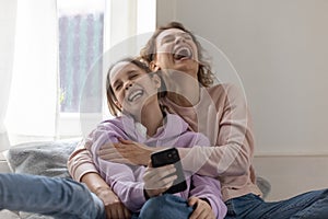 Overjoyed mother and teen daughter laugh using smartphone