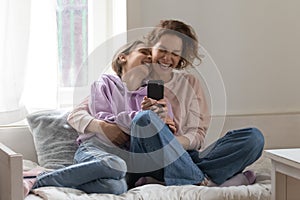 Overjoyed mother and teenage daughter having fun with smartphone