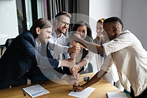 Overjoyed multiethnic businesspeople stack fists engaged in teambuilding