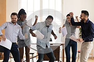 Overjoyed multiethnic employees dancing at workplace celebrating work success