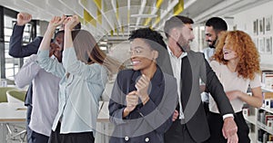 Overjoyed multiracial coworkers rejoicing corporate victory and having fun together. Cheerful young office staff dancing
