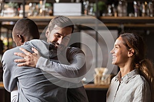 Overjoyed diverse friends embrace welcoming pal in bar photo