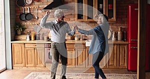 Overjoyed older senior couple dancing in kitchen.