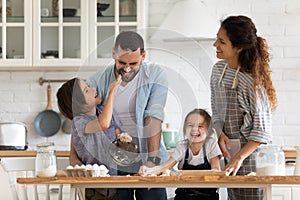 Overjoyed parents with little kids have fun cooking in kitchen