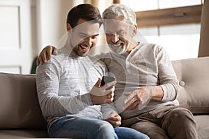Overjoyed senior dad and adult son using have fun smartphone