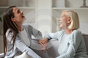 Overjoyed senior mom and adult daughter laugh talking at home