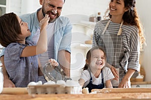 Overjoyed small children siblings spreading flour on laughing parents.