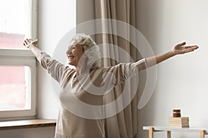 Overjoyed smiling mature woman standing with arms outstretched at home