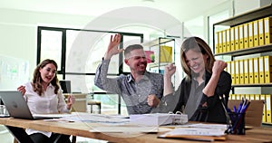 Overjoyed team of employees giving high five and celebrating success in office