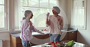 Overjoyed teen kid girl having fun with mom while cooking.