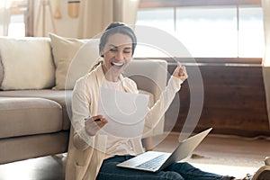 Overjoyed woman reading good news in letter, sitting on floor