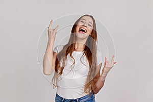 Overjoyed woman showing rock and roll hand sign and yelling, looking crazy with devil gesture.