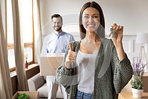 Overjoyed young 30s woman holding keys, showing thumbs up gesture.