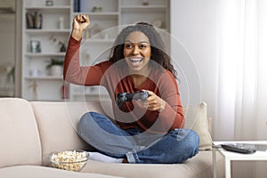 Overjoyed young black woman celebrating win while playing video games at home