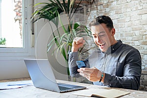 Overjoyed young businessman holding smartphone in hands, received message with good news, win notification. Happy lucky laughing