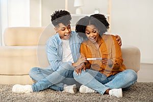 An overjoyed young couple sits on the floor with a positive pregnancy test