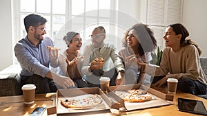 Overjoyed young diverse buddies eating ordered pizza for home party.